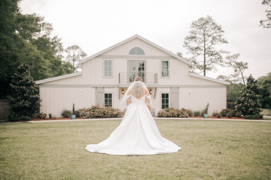 The bride is facing away from the camera, looking at the wedding venue behind her. She is wearing a white dress and veil.